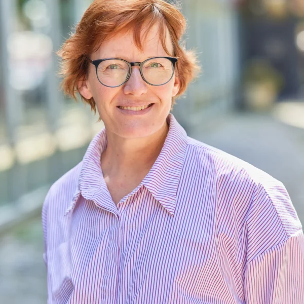 A woman with short red hair and glasses on a city street.