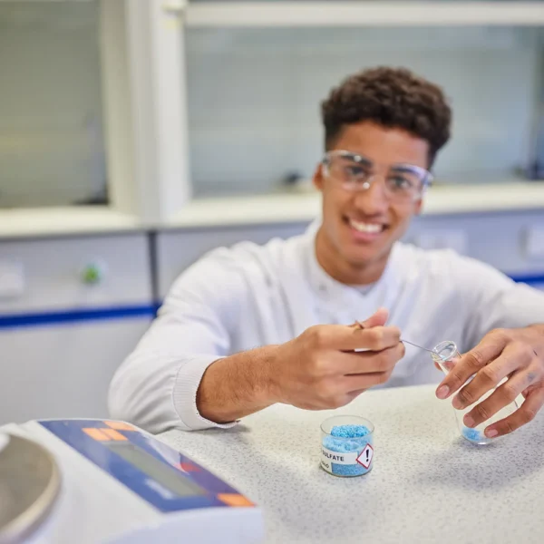 Young man in a lab coat and safety goggles handling a small object.
