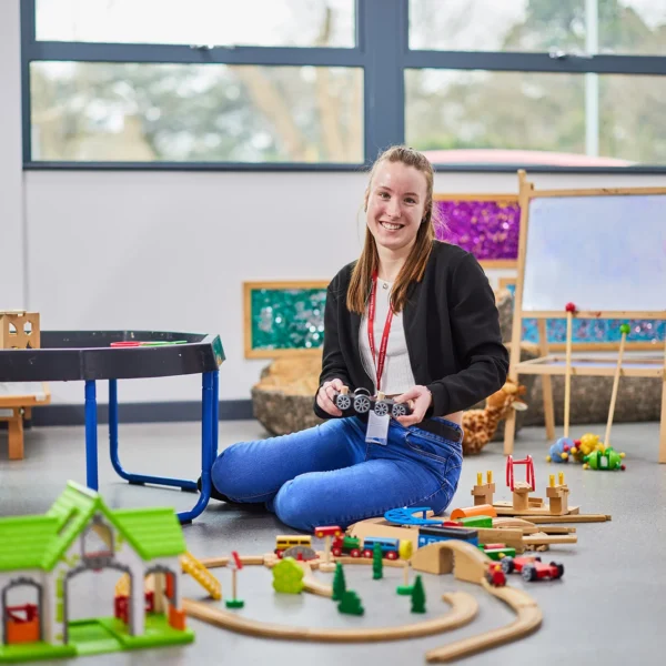 A woman sitting on the floor with toy train tracks and a toy house.