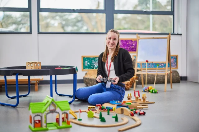 A woman sitting on the floor with toy train tracks and a toy house.