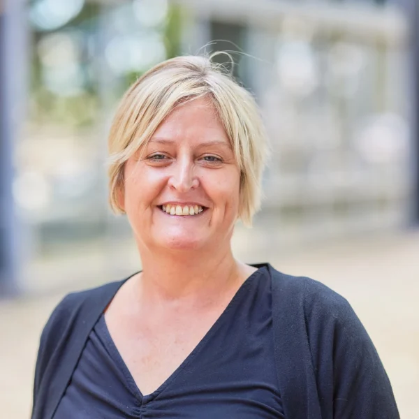 A smiling woman with short blonde hair wearing a dark blue top.