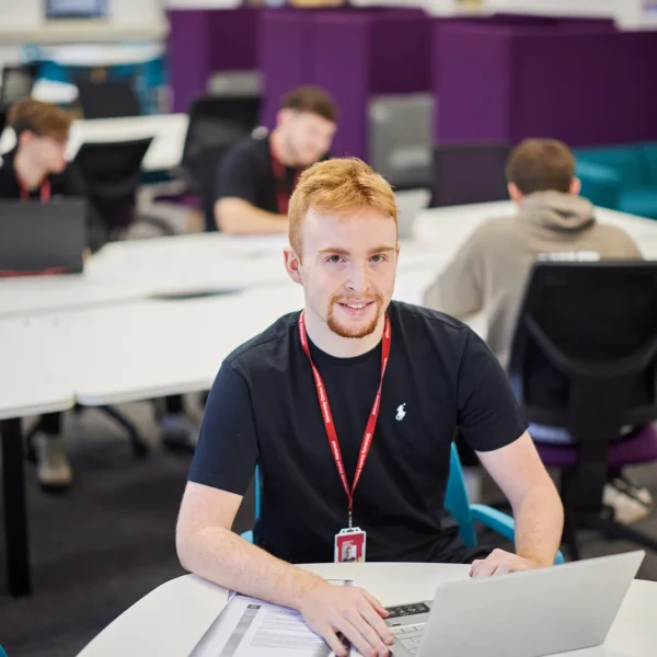 Young man with red hair using a laptop in a classroom setting.