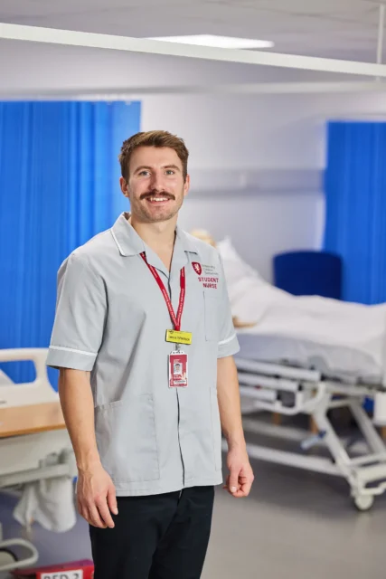 A man in a hospital setting wearing a light grey uniform.