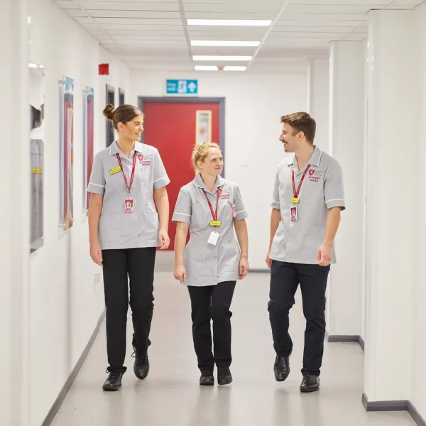 Three people walking down a hospital corridor, wearing medical uniforms and lanyards.