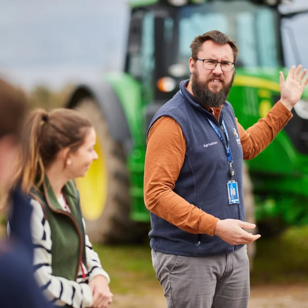 Man explaining something in front of a green tractor.