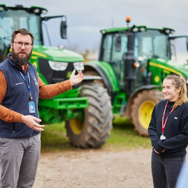 Man giving a presentation to a group of people with tractors in the background.