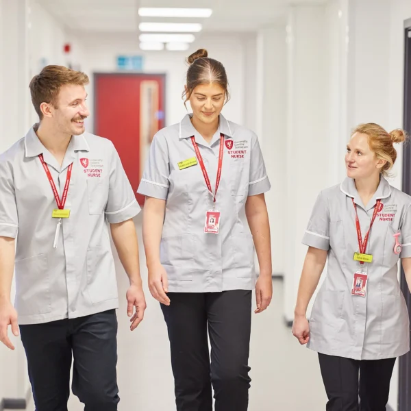 Three medical staff walking down a hospital corridor, smiling and wearing matching uniforms.