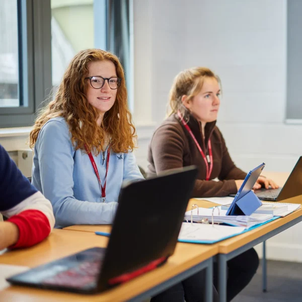 Three women sitting at desks with laptops in a classroom setting