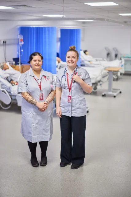 Two smiling nurses standing side by side in a hospital setting.