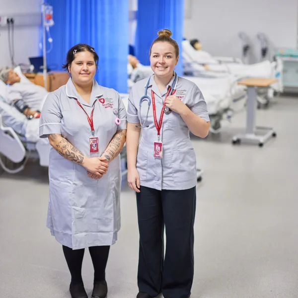 Two smiling nurses standing side by side in a hospital setting.