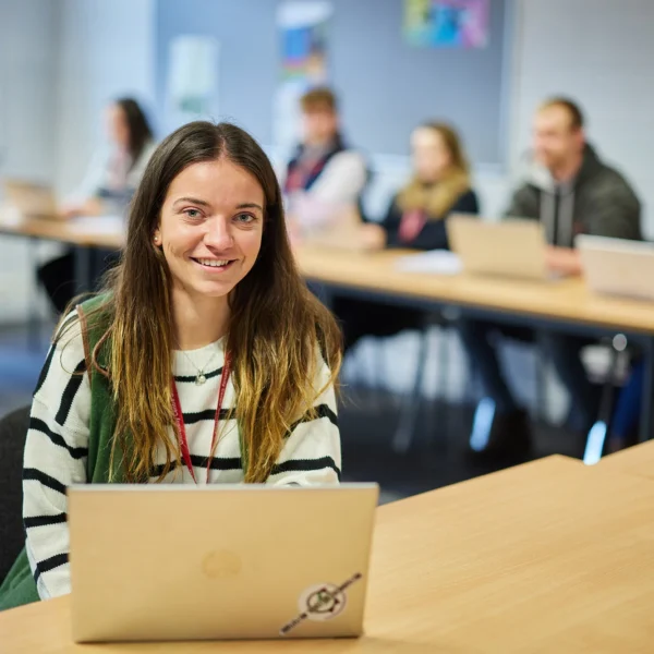 Young woman sitting at a desk with a laptop in a classroom setting.