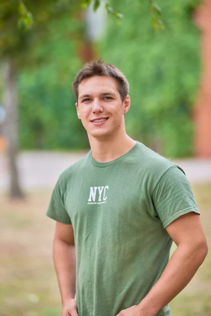 Young man wearing a green t-shirt with a white logo outside.