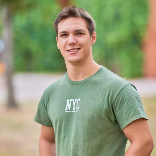 Young man wearing a green t-shirt with a white logo outside.