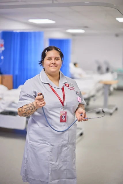 A female nurse in a hospital setting, holding a stethoscope.