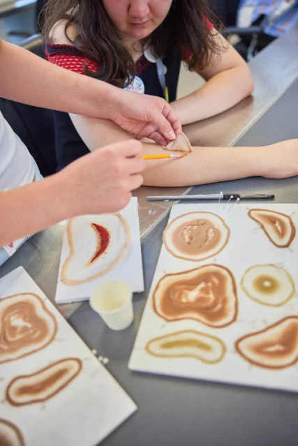 A person applying henna to another person's arm in a classroom setting.