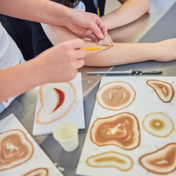 A person applying henna to another person's arm in a classroom setting.