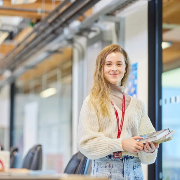 Young woman with long blonde hair standing in an office holding a tablet.