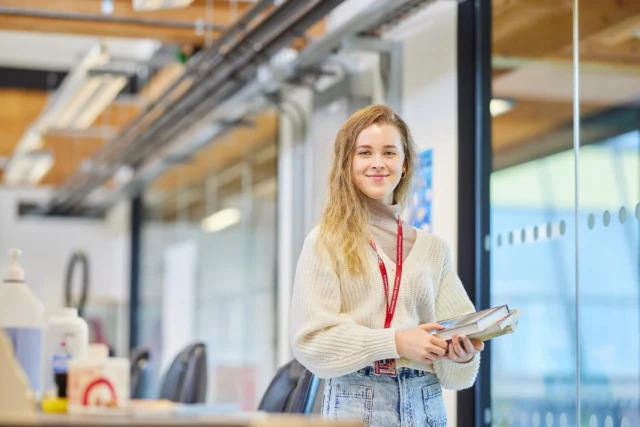 Young woman with long blonde hair standing in an office holding a tablet.