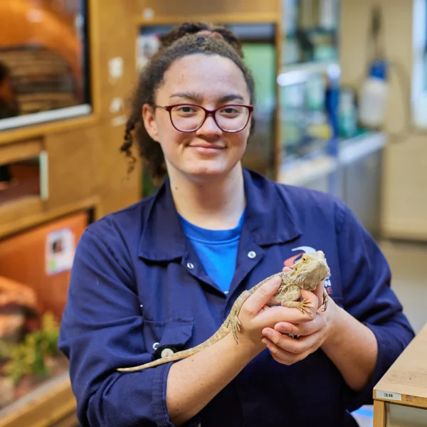 A woman wearing a blue jumpsuit holding a lizard in her hands.