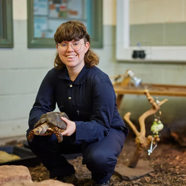 A woman crouches down holding a lizard in her hands.