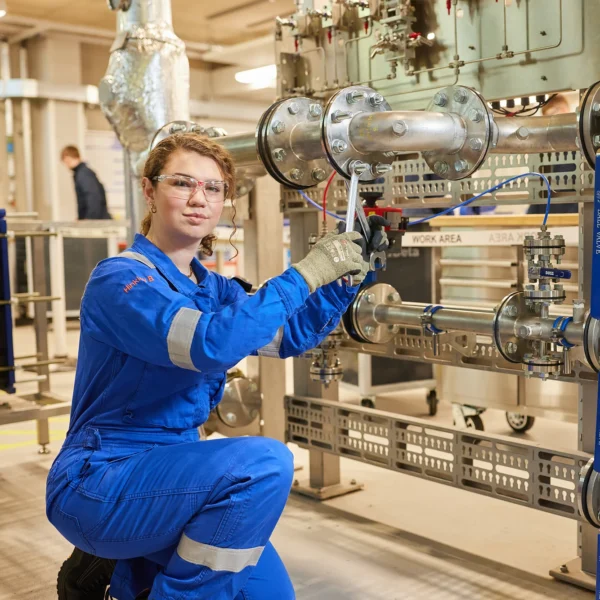 A worker in blue overalls inspecting industrial pipes.