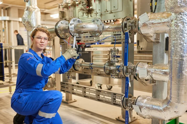 A worker in blue overalls inspecting industrial pipes.