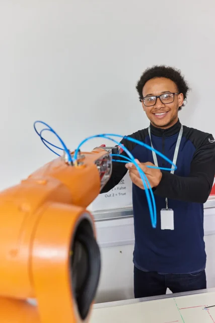 Young man connecting blue wires to an orange machine, smiling.