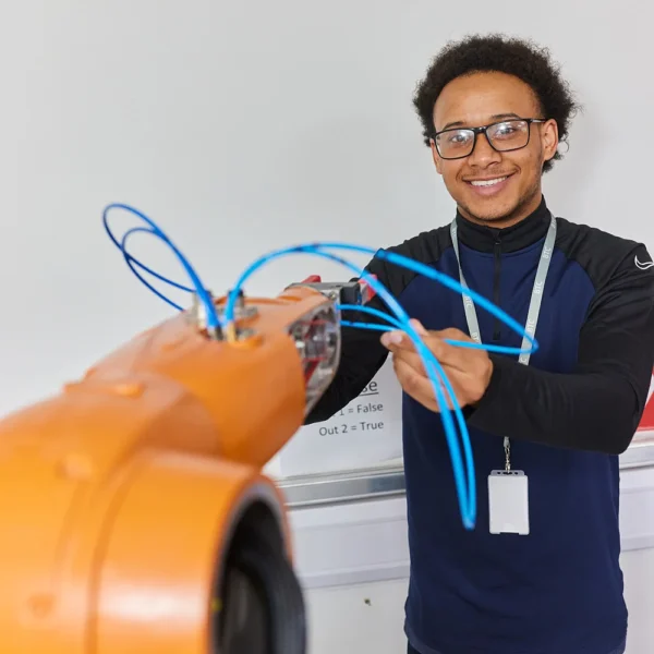 Young man connecting blue wires to an orange machine, smiling.