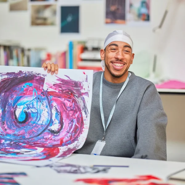 Man holding a colorful painting in an art room.