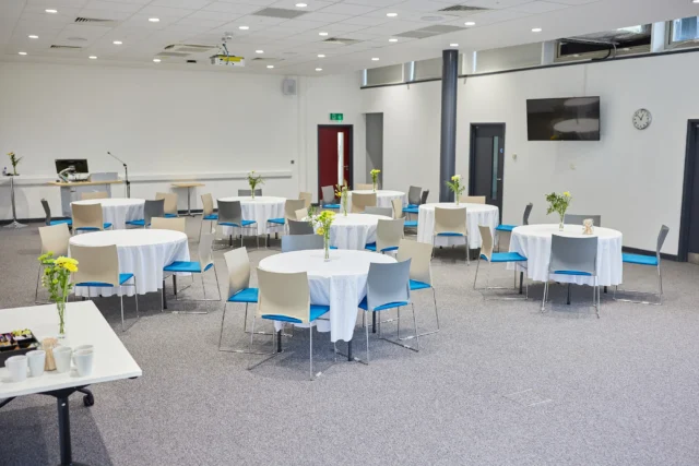 A dining area with multiple tables and chairs, featuring white tablecloths and blue accents.