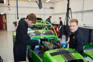 Two mechanics working on a green racecar in a garage.