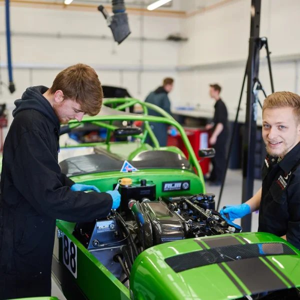 Two mechanics working on a green racecar in a garage.