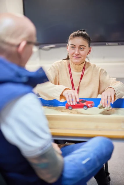 Woman sitting at a table with a red object in a blue tray, looking at a man.