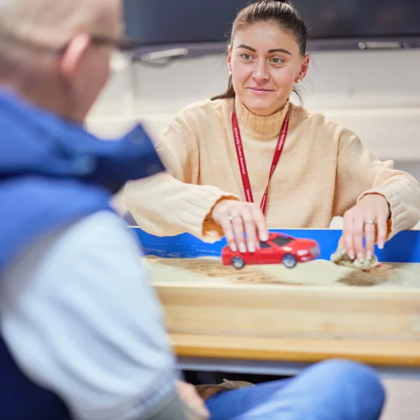Woman sitting at a table with a red object in a blue tray, looking at a man.