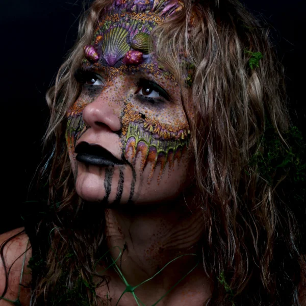 A woman with shells and scales painted and moulded onto her face and body.