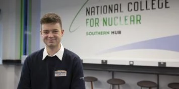 A young man standing in front of a sign for the National College for Nuclear Southern Hub.