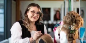 Woman with long brown hair and glasses smiling while combing hair