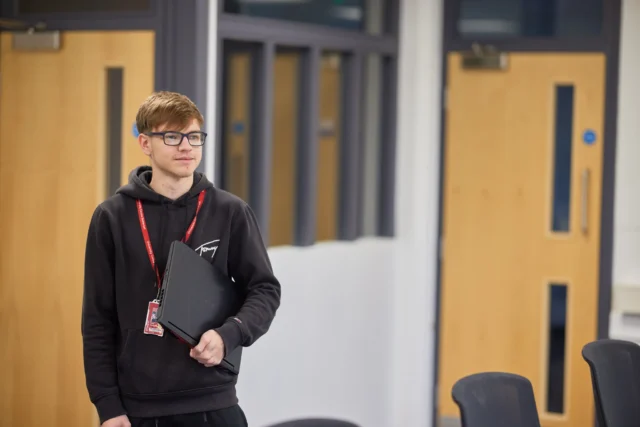 Teenager holding a laptop in a room with wooden doors.