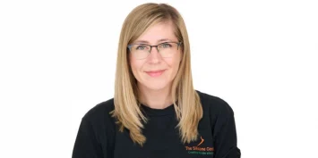 A smiling woman with glasses and blonde hair wearing a black shirt.