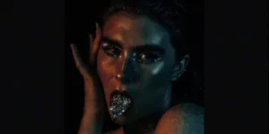 A woman with her hand on her face and silver glitter on her lips.