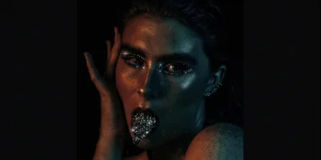A woman with her hand on her face and silver glitter on her lips.