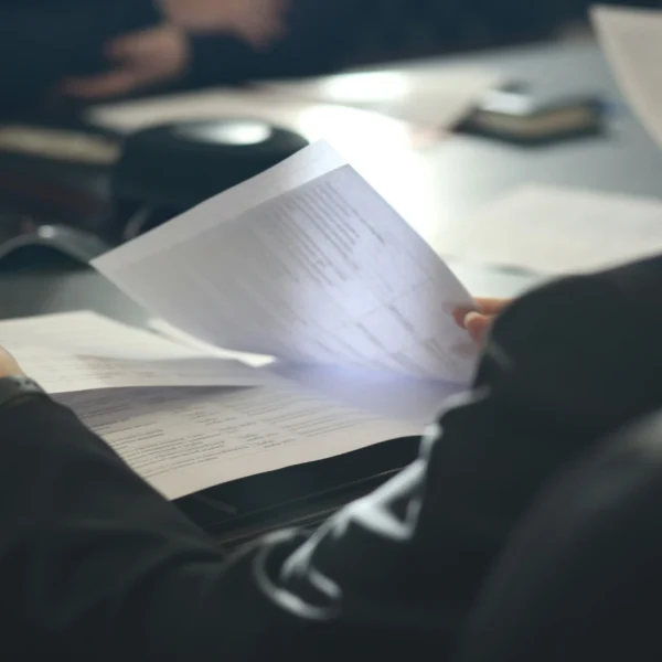 A person in a dark shirt holding a paper and reviewing documents.