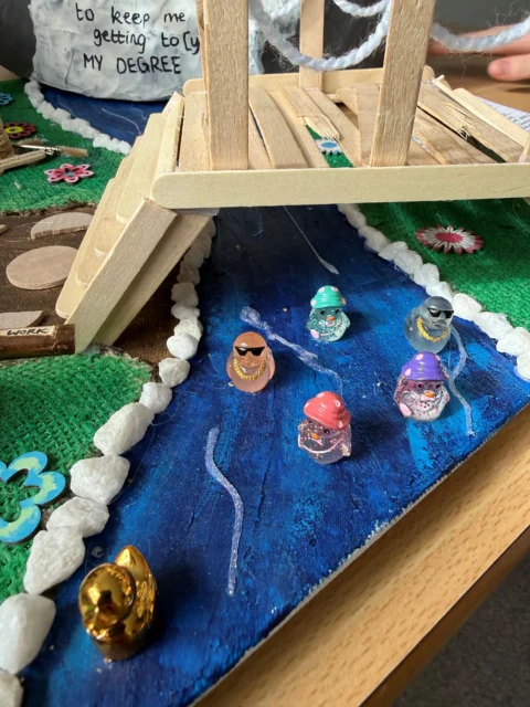 A child's hands on a craft bridge over water with jellyfish and sea creatures.
