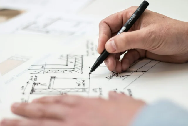 A person drawing on architectural plans with a pen.