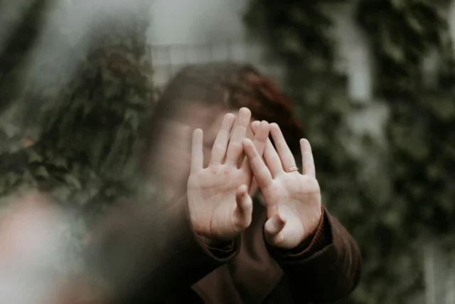 A person covering their face with their hands, with a blurred background.