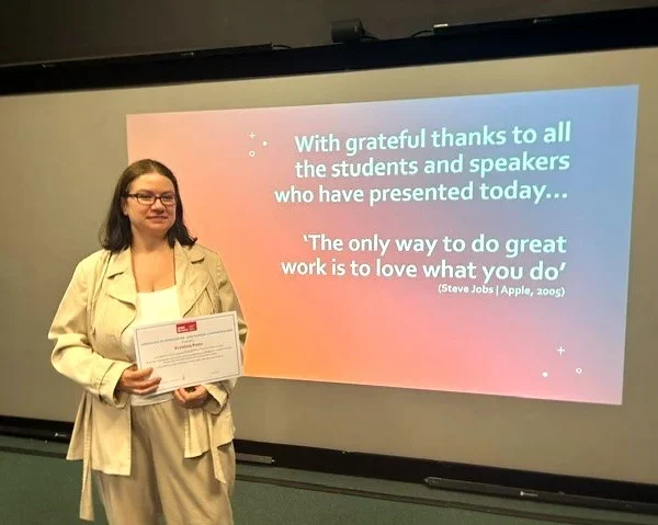 Krystyna stands holding a certificate in front of a presentation slide at the UWE Bristol conference with a thank-you message and an inspirational quote by Steve Jobs.