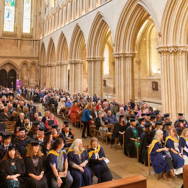 A large crowd of people gathered in a grand cathedral for a formal event, with many wearing academic regalia.