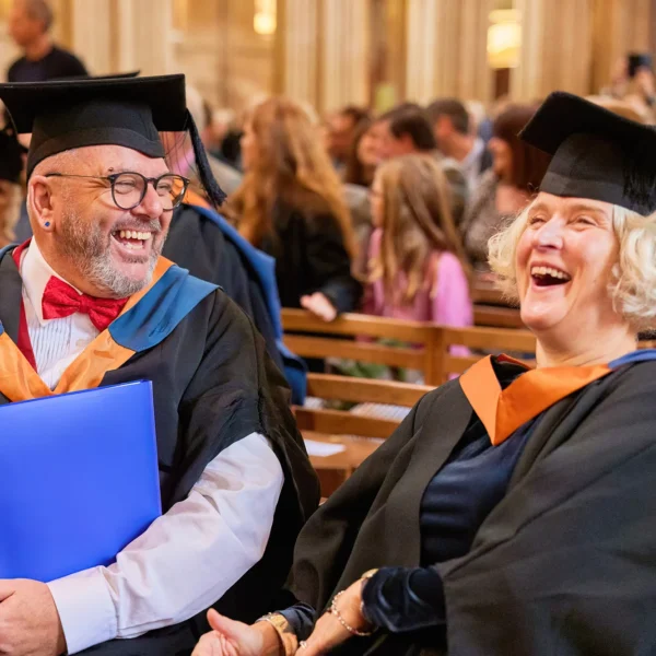 A man and woman in academic regalia smiling at each other.