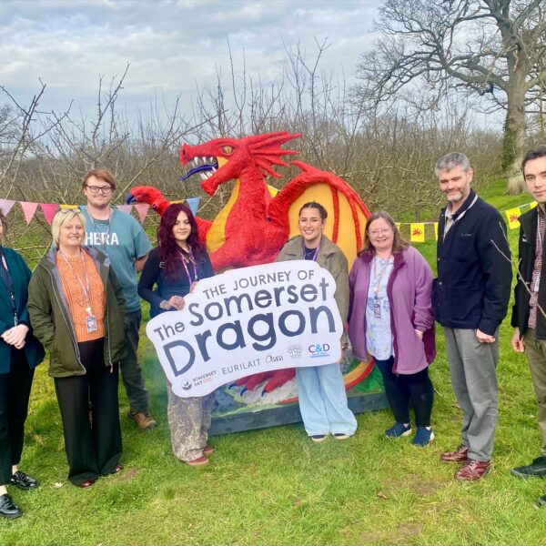 Group of people standing with a large red dragon and a sign that reads The Somerset Dragon.
