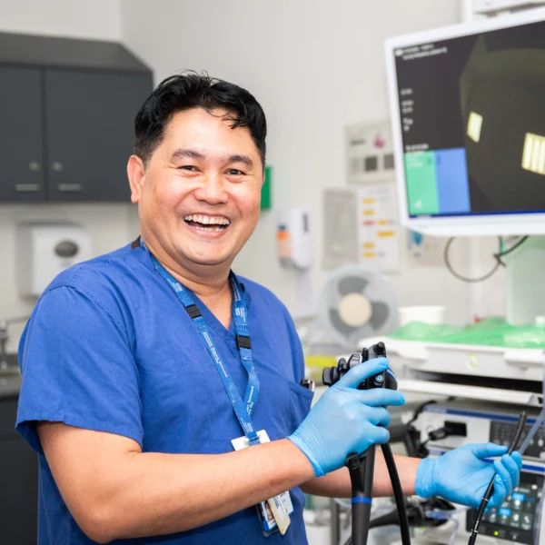 A smiling medical professional in blue scrubs and gloves holds an endoscope in a modern diagnostic room.